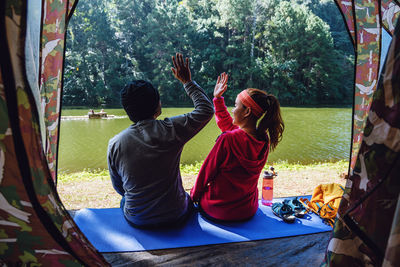 Rear view of people sitting on mat by lake