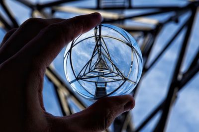 Cropped hand of man holding crystal ball under electricity pylon