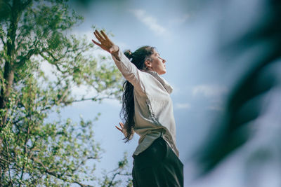 Low angle view of woman standing by tree against sky