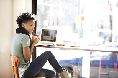 Happy woman having coffee while using laptop computer in cafe