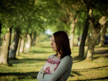 Thoughtful woman with arms crossed standing on pathway amidst trees at park