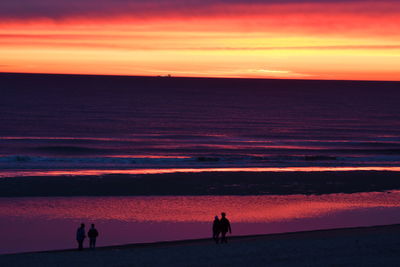 Silhouette people at beach against sky during sunset