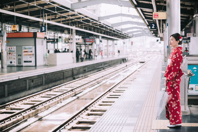 Side view of woman with umbrella standing at railroad station