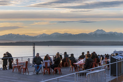 People sitting by sea at restaurant during sunset