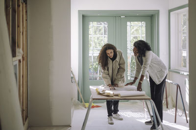 Female design professional discussing over blueprint with client at under construction apartment