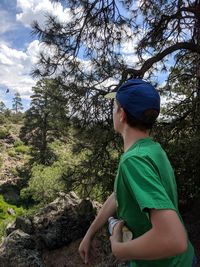 Boy looking away while standing against tree