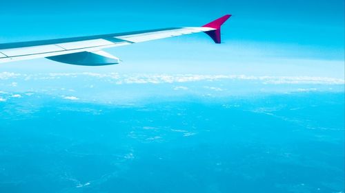 Aerial view of airplane flying over sea against blue sky