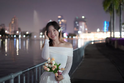Portrait of young woman standing against illuminated city at night