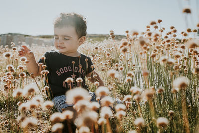 Cute girl sitting amidst flowers against sky