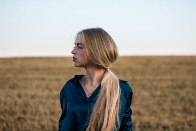 Thoughtful young woman standing on field against clear sky