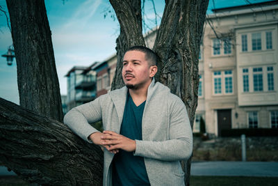 Portrait of young man standing on tree trunk