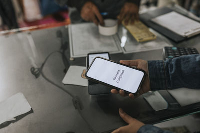 Hand of woman making contactless payment through smart phone in workshop