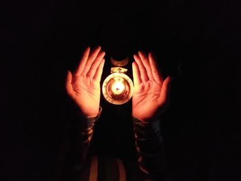 Midsection of person holding illuminated lamp against black background