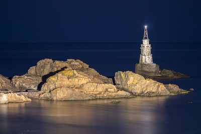 Rocks and lighthouse by the sea against the sky at night
