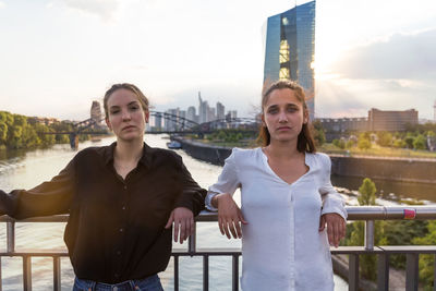 Portrait of young women standing against railing on bridge in city