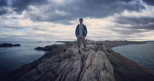 Full length of man standing on cliff amidst seas against cloudy sky