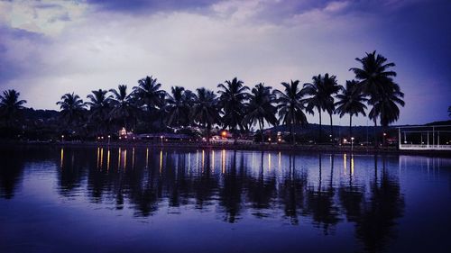 Palm trees by lake against sky at dusk