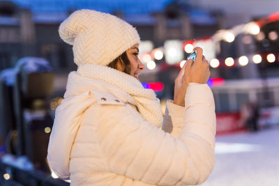 Side view of woman holding smart phone during winter