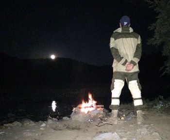 Rear view of man standing against illuminated fire at night