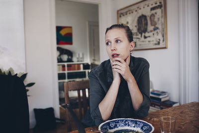 Thoughtful woman sitting at dining table in room