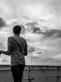 Rear view of man standing against cloudy sky