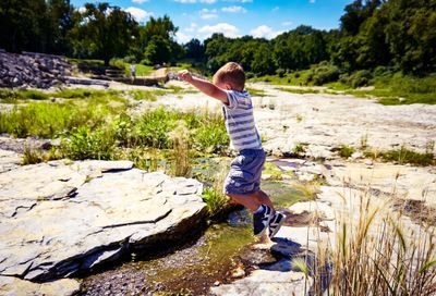 Boy standing on rock by river against sky