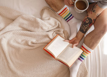  close up of man legs with a book drinking coffee in bed at home in the morning.