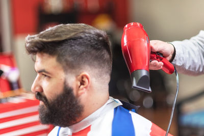 Cropped hand of barber holding hair dryer by male customer hair in salon