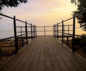 Empty footbridge against sky at sunset