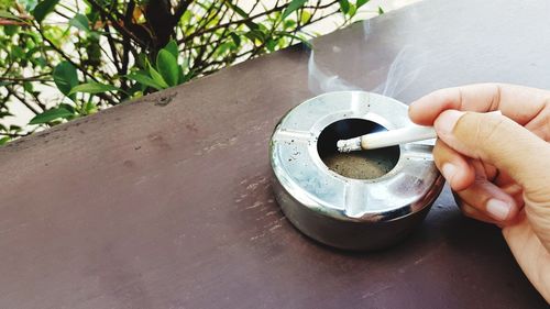 Cropped hand of man holding cigarette by ash tray