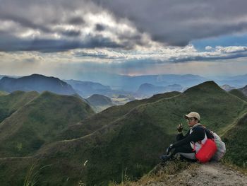 Woman sitting on mountain against sky