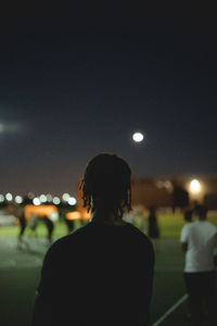 Rear view of man standing on illuminated city against sky at night