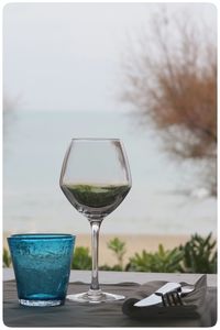 Close-up of wineglass on table against beach