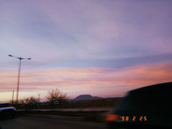 Cars on street against sky at sunset