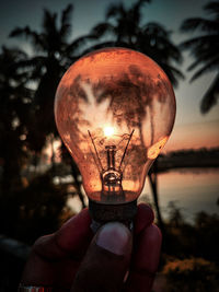 Close-up of hand holding light bulb against sky