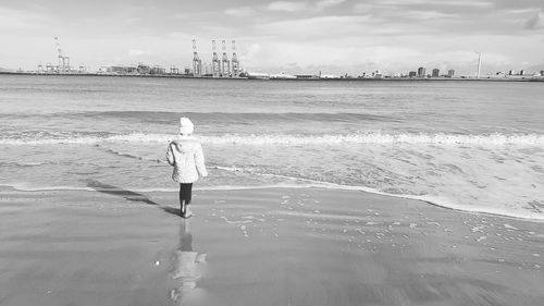 Rear view of woman standing on beach against sky