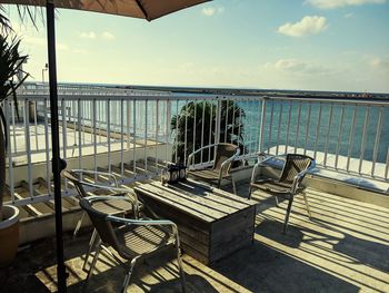 Empty chairs and table by sea against sky