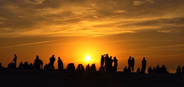 Silhouette people on beach against sky during sunset