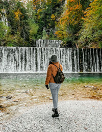 Rear view of female hiker standing in front of waterfall in autumn forest