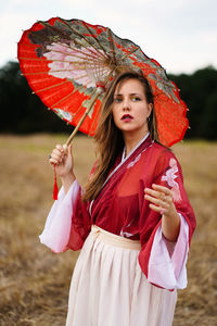 Thoughtful young woman holding umbrella while standing on land