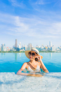 Young woman wearing sunglasses in swimming pool against sky