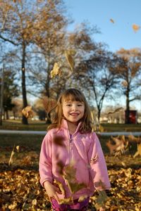 Full length portrait of girl throwing leaves on field