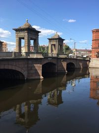 Arch bridge over river by buildings against sky