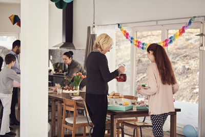 Multi-generation family arranging food and drink on table during birthday party