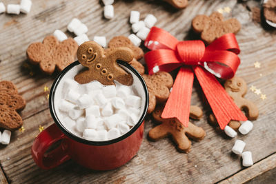 Ginger man in a cup of cocoa with a big red bow on a wooden background, top view. 