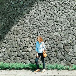 Full length of woman standing against stone wall