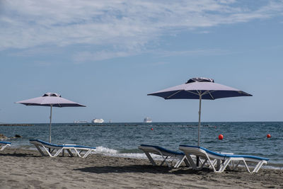 Empty sunlounger and waiting cruise ships at shoreline of limassol during lockdown at sunny day.