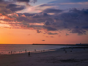 Silhouette people on beach against sky during sunset