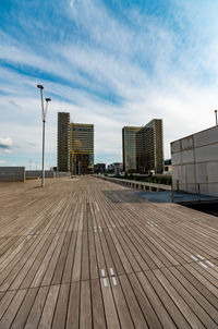 Empty footpath amidst buildings in city against sky
