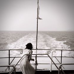 Woman standing on railing by sea against clear sky